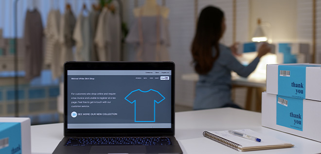 Computador exibindo e-commerce de roupas e ao fundo profissional trabalhando em loja